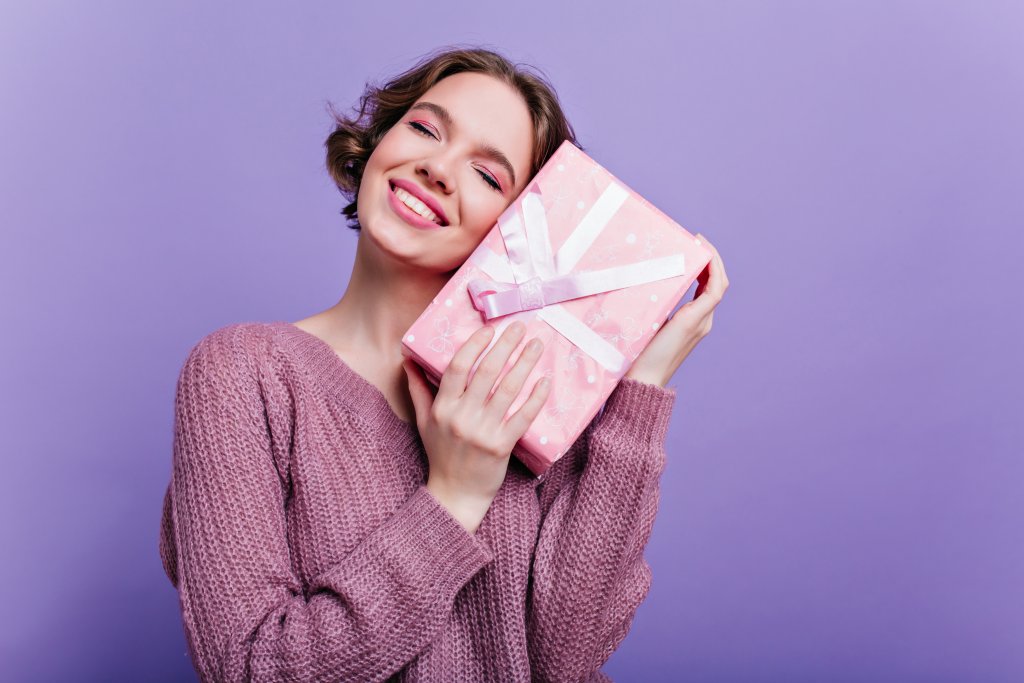 pleased-lady-with-glamorous-makeup-posing-with-new-year-gift-on-purple-wall-dreamy-short-haired-girl-standing-with-eyes-closed-holding-birthday-present.jpg
